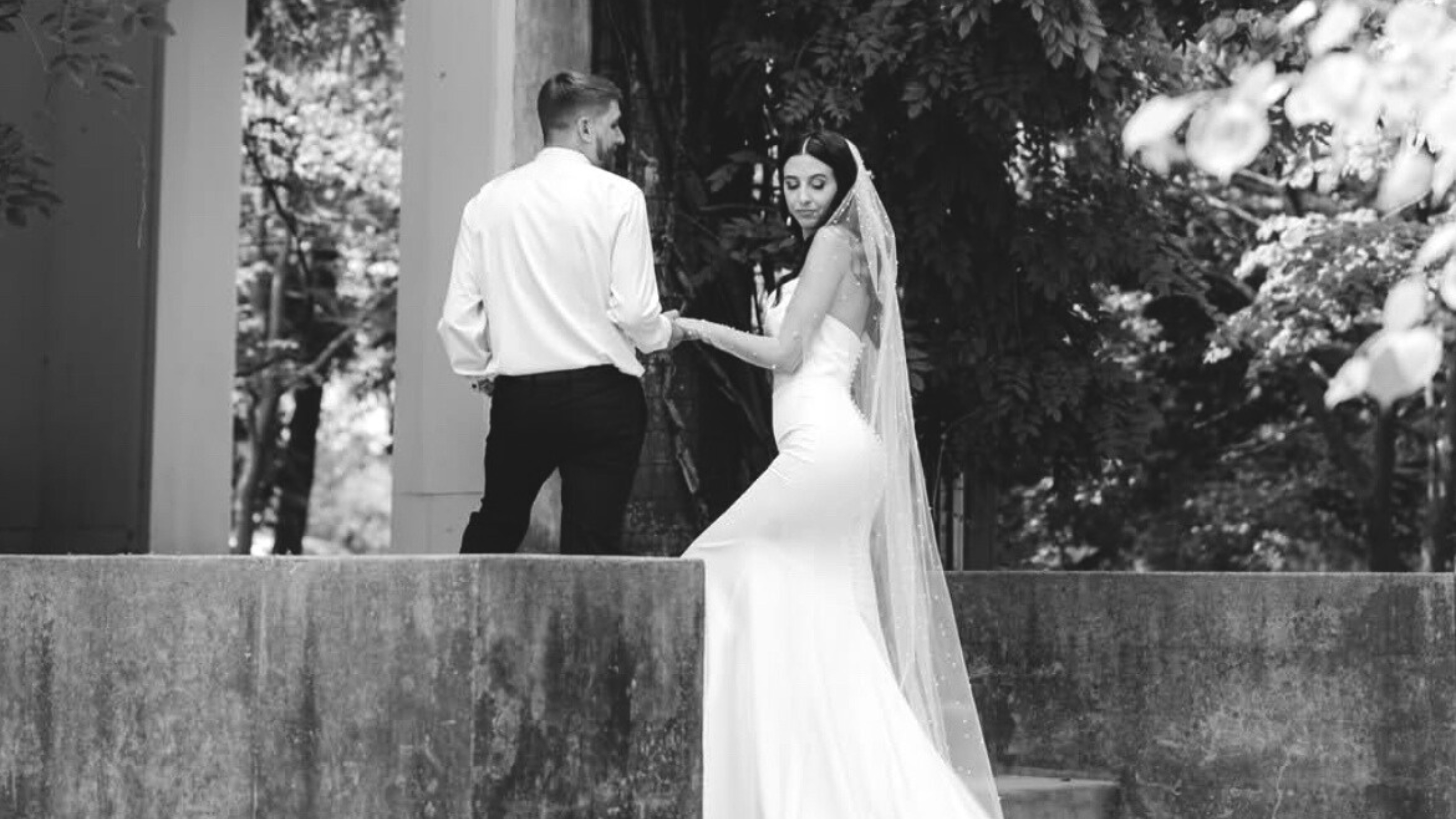 a black and white image of a groom leading his bride up a set of stairs
